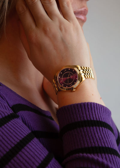 The elegant gold and purple timepiece worn on a wrist, showcasing its rich jewel-toned colour.