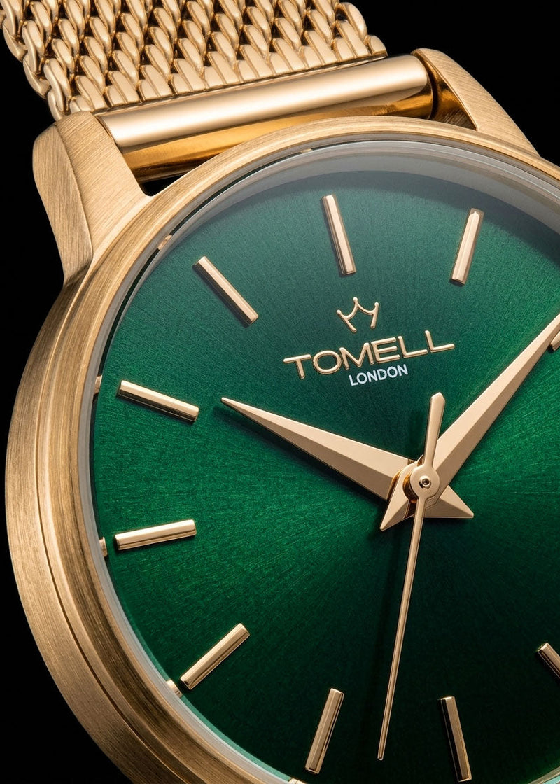 Gold watch with green face and 'Tomell London' branding on a black background