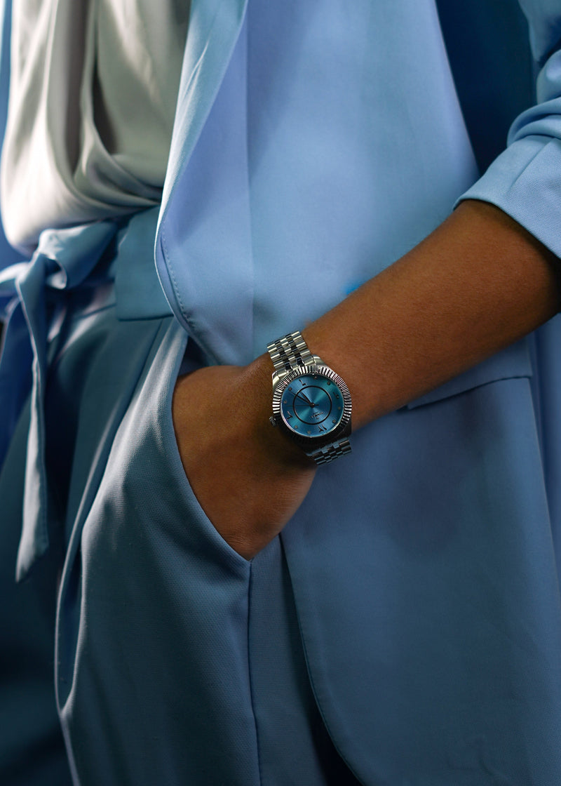 Close-up of an exceptional azure-blue sunray dial featuring bold Arabic numerals. This hand-picked artifact vibrates with a cool metallic integrity, where brilliant diamond accents act as flickering points of light against a deep-pigment oceanic background, engineered to feel like a formidable extension of your pulse.