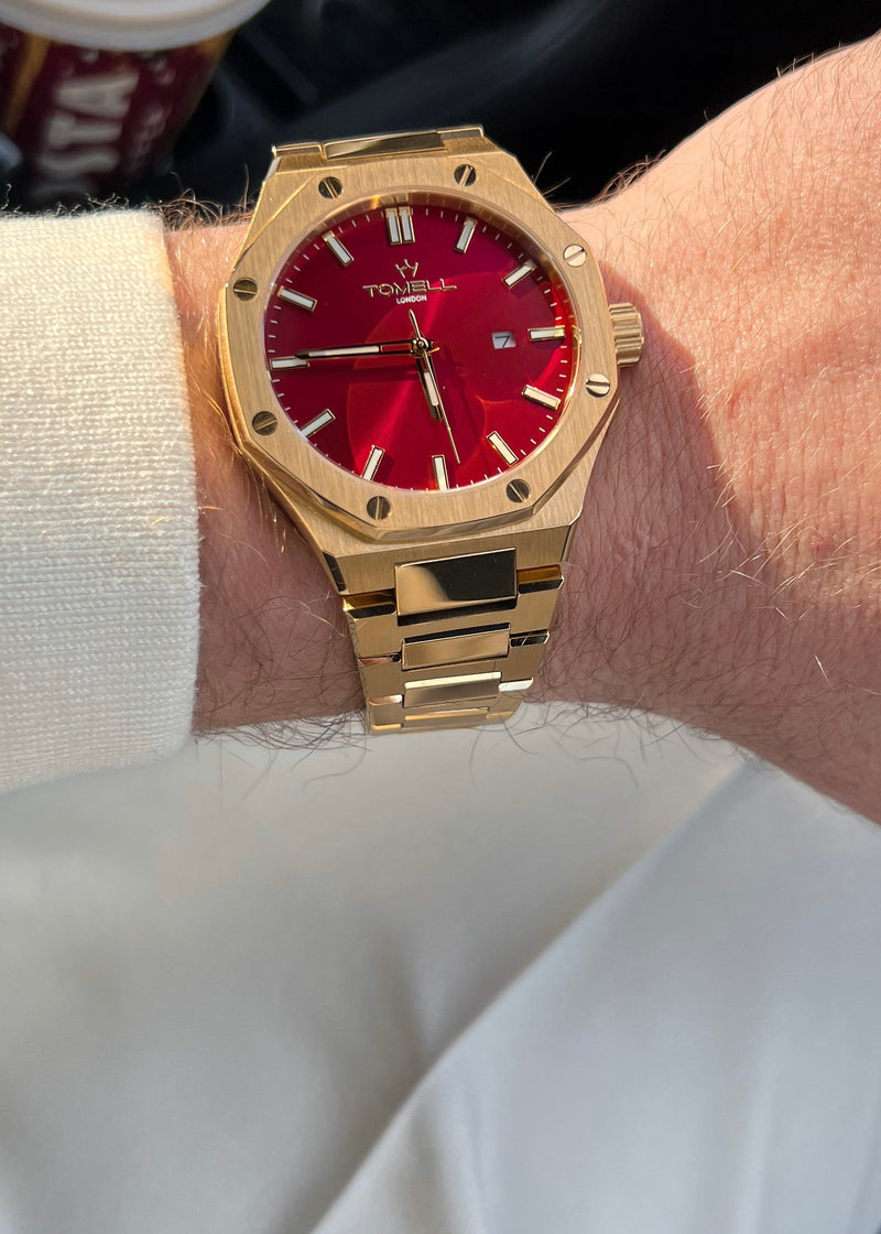 Gold watch with a red face on a wrist, with a blurred background of a car interior.