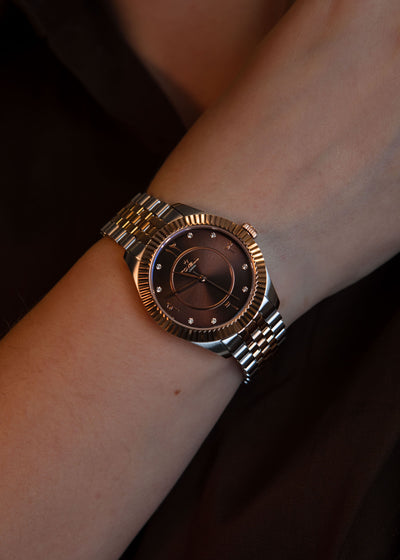 Close-up of the watch dial highlighting the rose gold hands and diamond marker on the chocolate face.