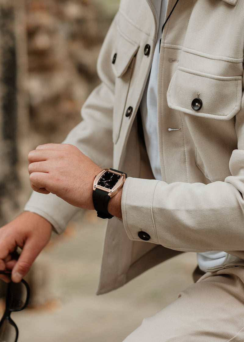 A vivid, high-relief photograph of a Tomell London men's watch, showcasing the razor-sharp architectural defiance of its square rose-gold casing. The matte black rubber strap provides a visceral, low-profile tension against the steeled warmth of the frame, marking it as a formidable signature of modern power.