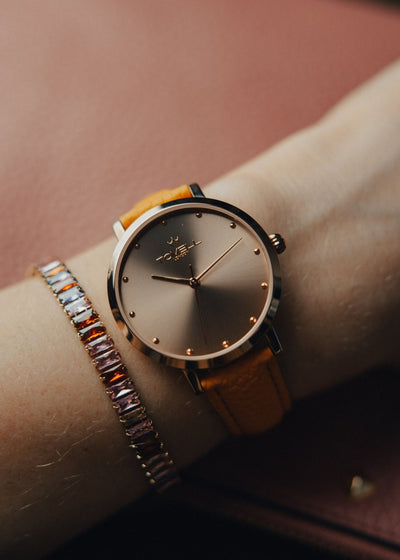 Wrist wearing a watch with a brown strap and gold accents