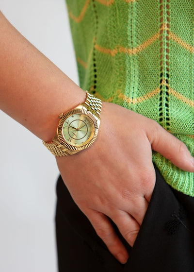 Stylish gold watch with mint face worn on the wrist, showing the side profile and crown.